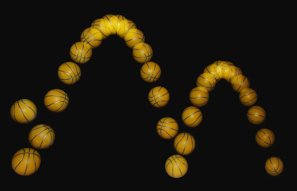 A stroboscopic photograph of a basketball bouncing from left to right against a black background. The images of the ball trace out two arches, the second lower than the first. The images are evenly spaced horizontally but crowd together at the top of each arch and spread apart lower down.