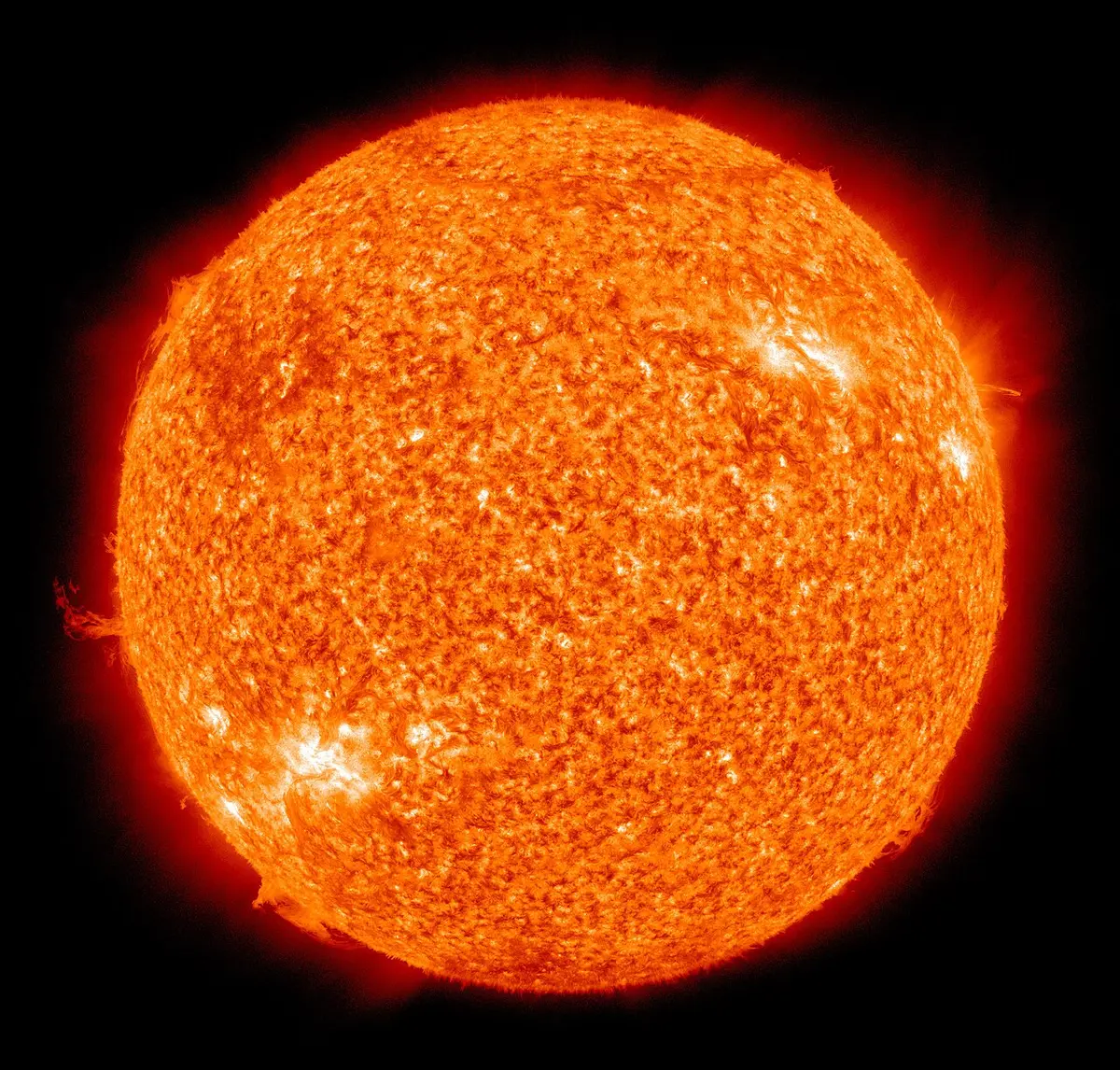 The Sun photographed in extreme ultraviolet light and coloured orange-yellow. Its surface is mottled, with bright active regions, and loops and wisps of glowing gas rise from its edge.